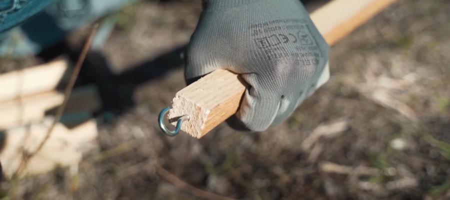 main avec un gant de chantier qui tient un tasseau avec un crochet vissé au bout