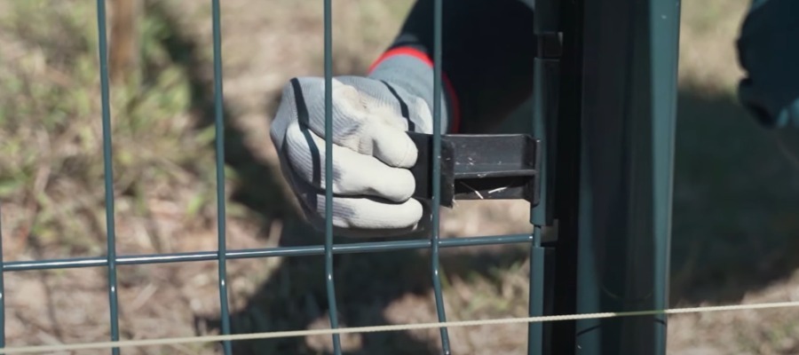 main avec gant de chantier qui pose une cale de tension entre les fils rigides du grillage